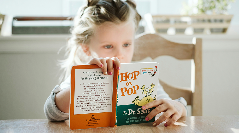 A young girl sat at the table reading a Dr Seuss book